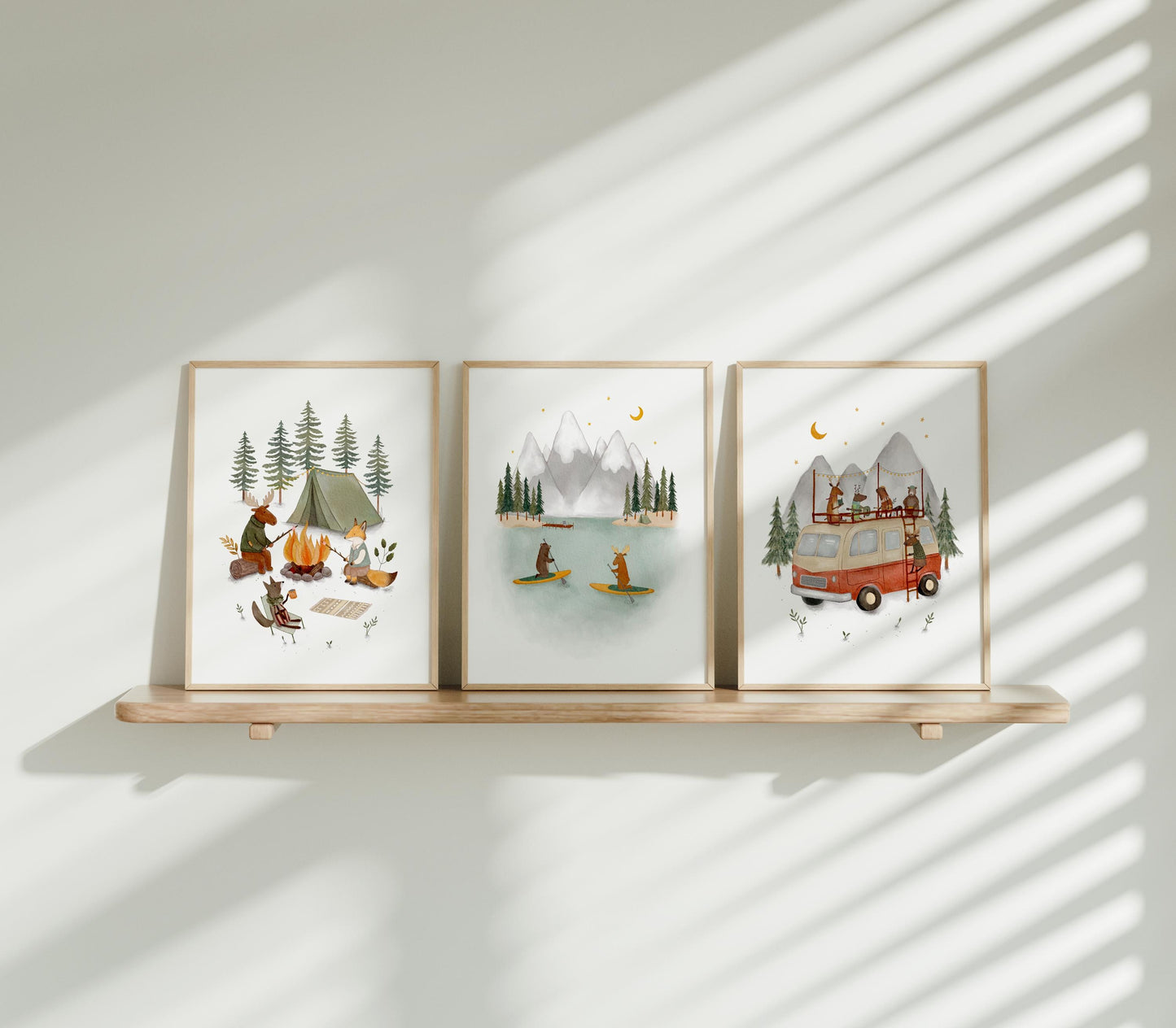 three framed pictures on a wooden shelf, each depicting different scenes related to camping and outdoor activities.