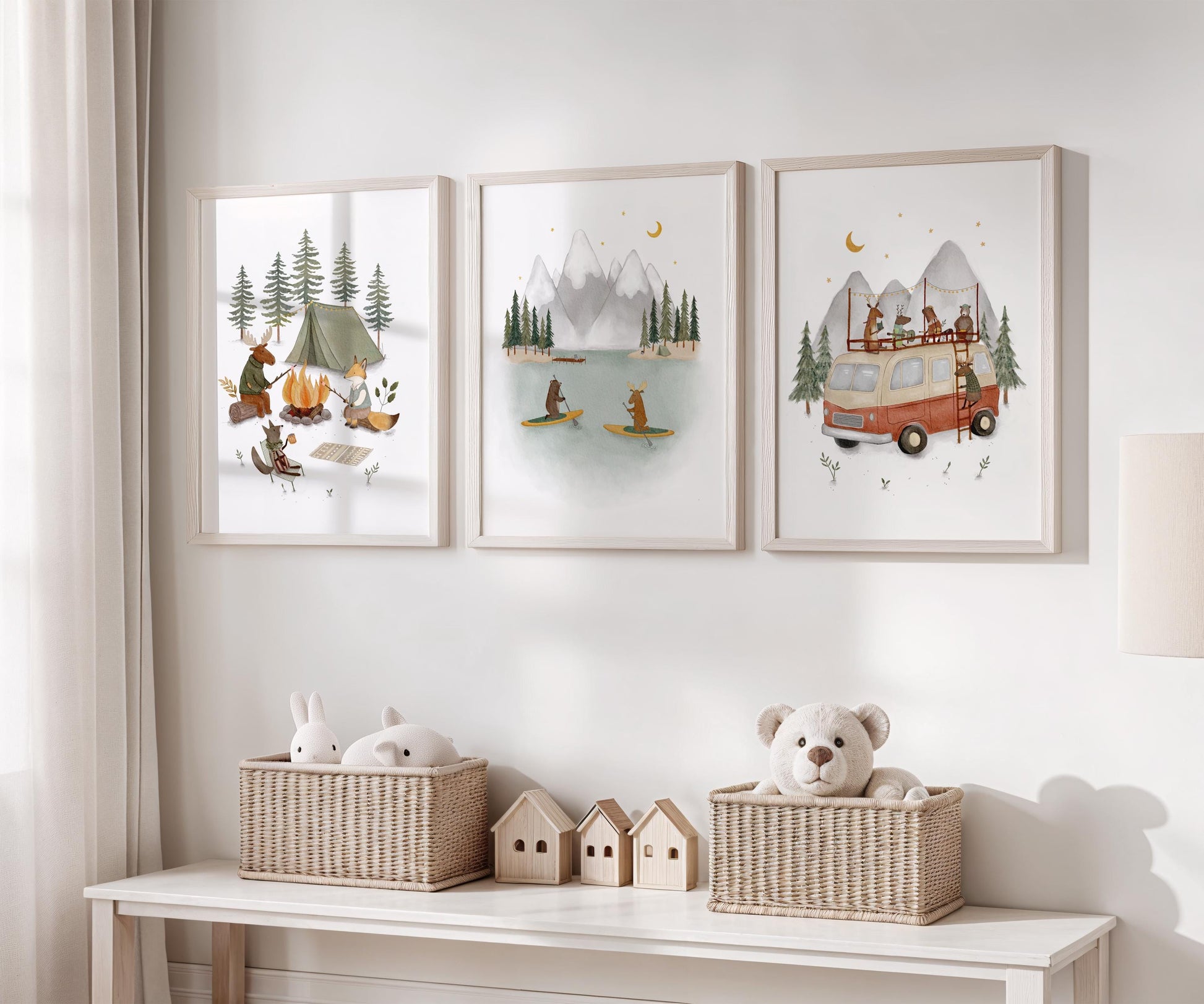 three framed pictures hanging on a wall, each depicting a different scene related to camping and nature. Below the pictures, there are two wicker baskets containing stuffed animals, including a teddy bear.