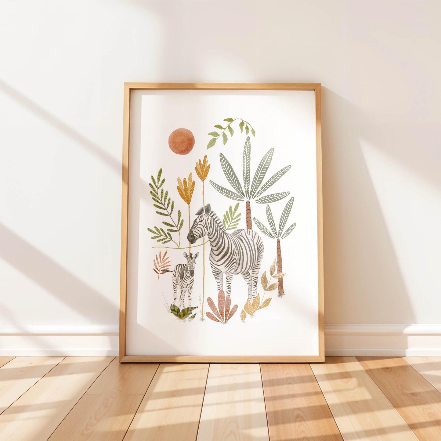 A single framed art print leaning against a white wall, featuring a hand-painted watercolor illustration of a mother zebra and her foal standing in a boho jungle landscape under the sun.